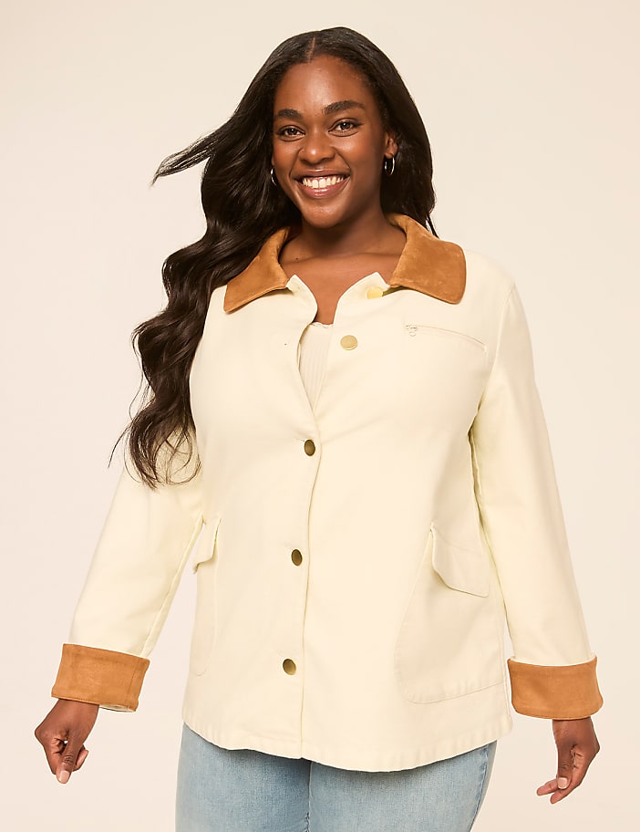 A smiling woman in a cream jacket with brown accents stands against a plain, light-colored background.