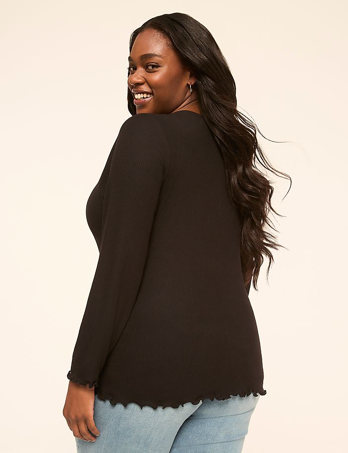 A smiling woman in a black ribbed top stands against a plain, light-colored background.