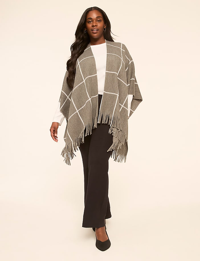 A woman in a plaid poncho and black pants stands against a plain, light-colored background.