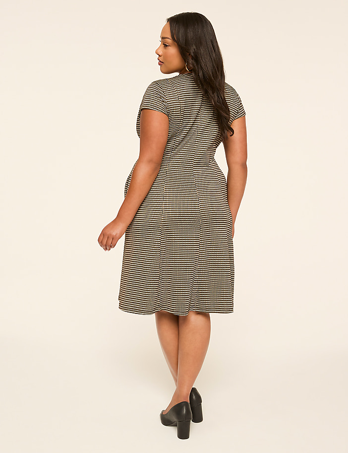 A woman in a striped dress stands against a plain, light-colored background.