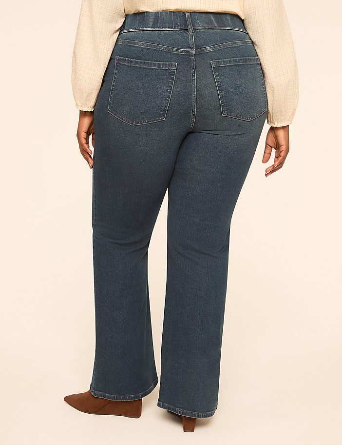 A person wearing dark wash bootcut jeans and brown boots stands against a plain, light-colored background.