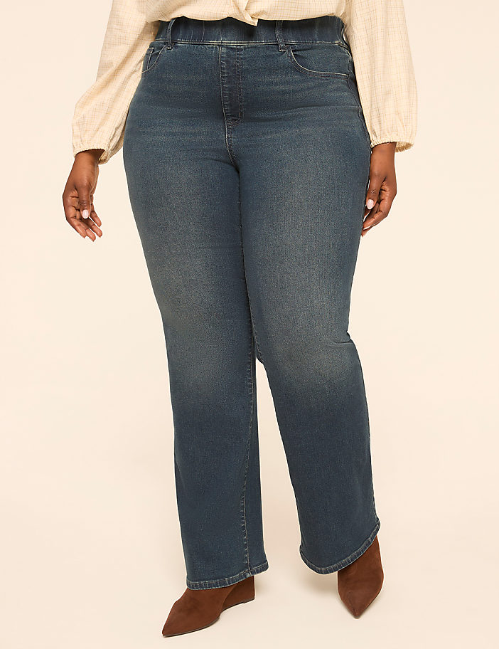 A person in blue jeans and a cream-colored top stands against a plain, light-colored background.