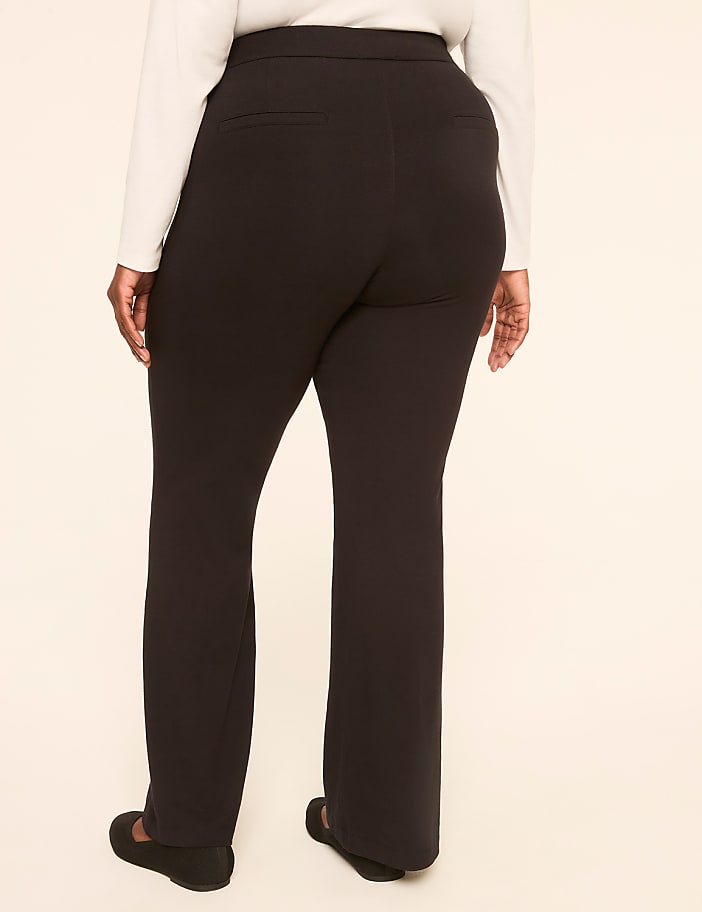 A person wearing black pants and a white shirt stands against a plain, light-colored background.