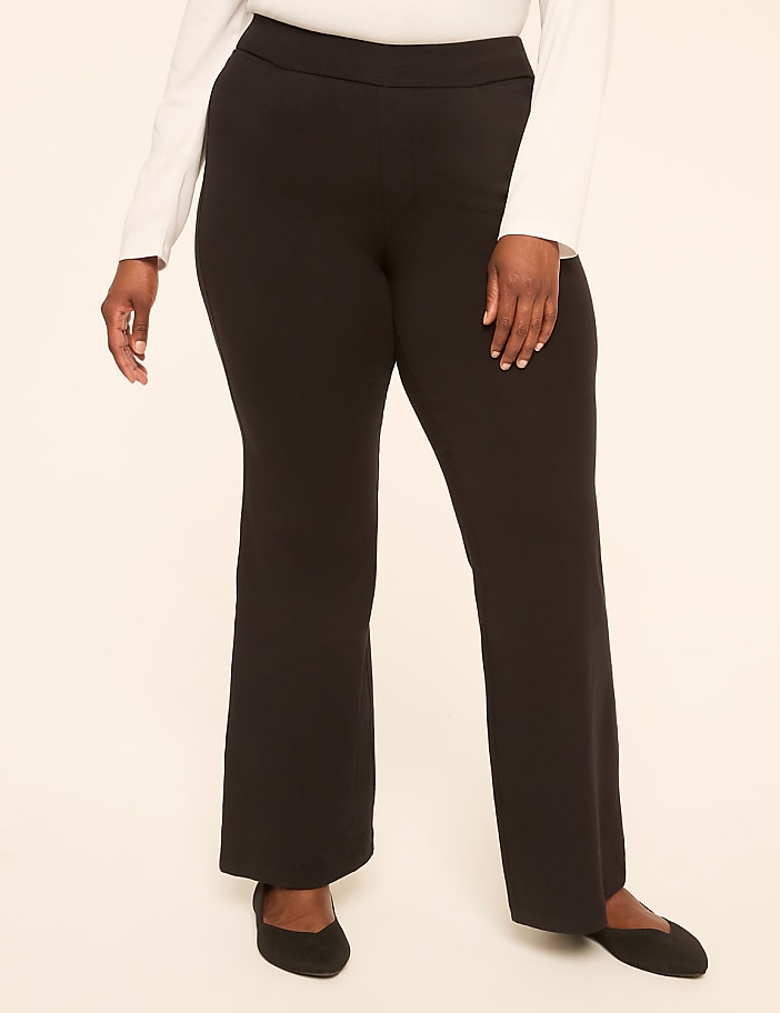 A person wearing black flared pants and black flats stands against a plain, light-colored background.