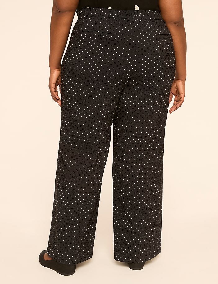 A person wearing black polka dot pants stands against a plain, light-colored background.