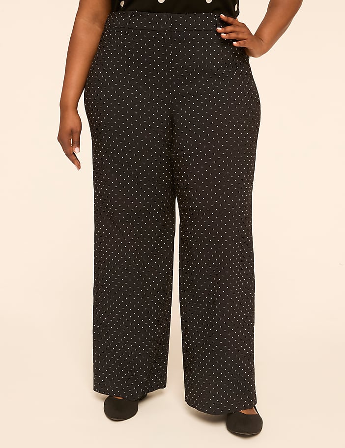 A person stands in polka dot pants and black shoes against a plain, light-colored background.