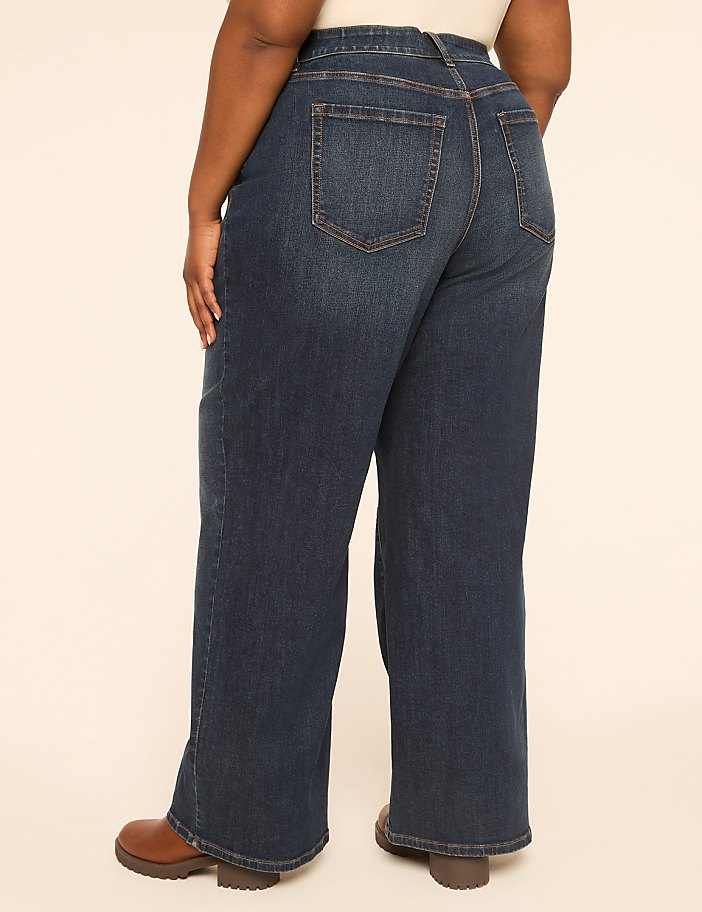 A person wearing dark wash wide-leg jeans and brown boots stands against a plain, light-colored background.