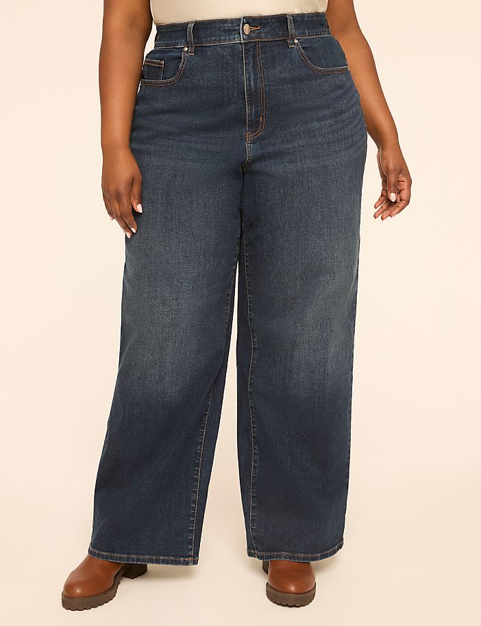 A person stands in dark wash wide-leg jeans and brown boots against a plain, light-colored background.