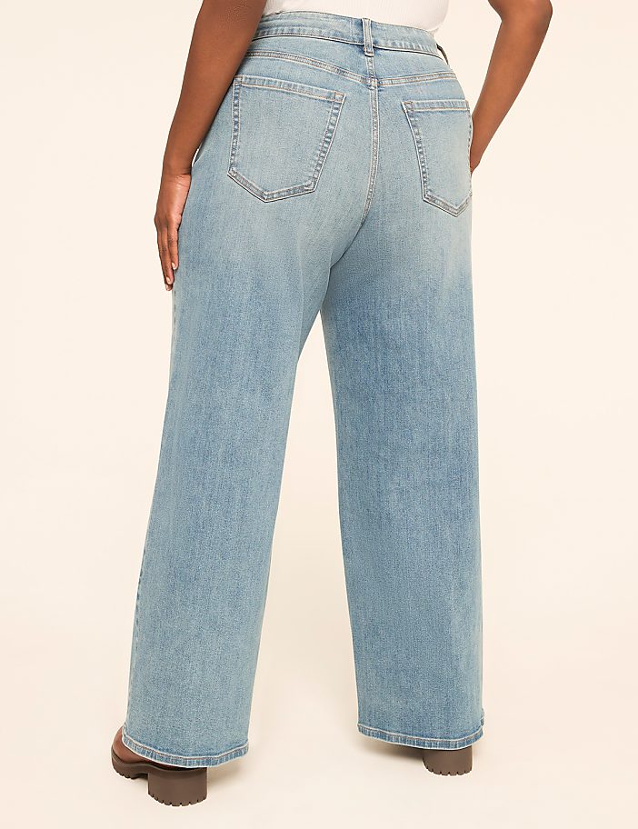 A person wearing light-wash wide-leg jeans stands against a plain, light-colored background.