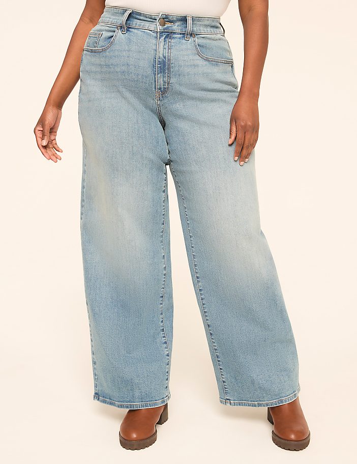 A person wearing light-wash wide-leg jeans and brown boots stands against a plain, light-colored background.