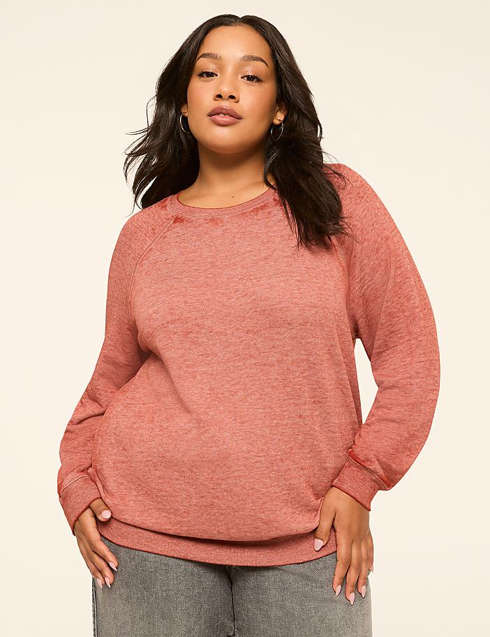 A woman in a coral-colored sweatshirt stands against a plain, light-colored background.