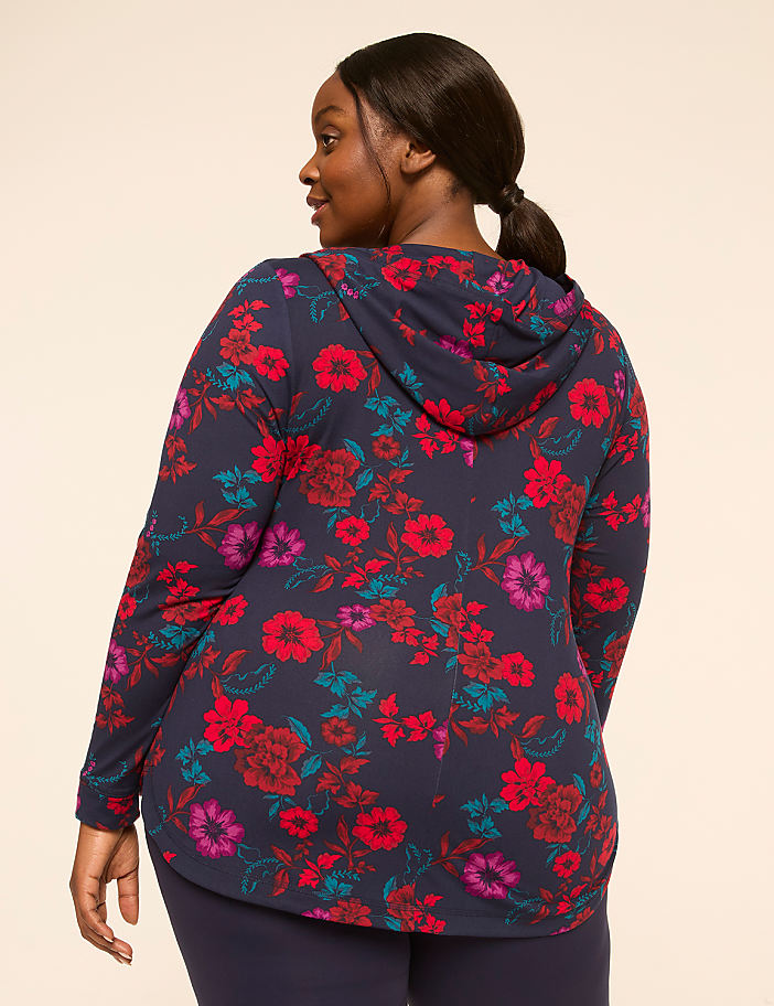 A woman in a floral hoodie and leggings stands against a plain, light-colored background.