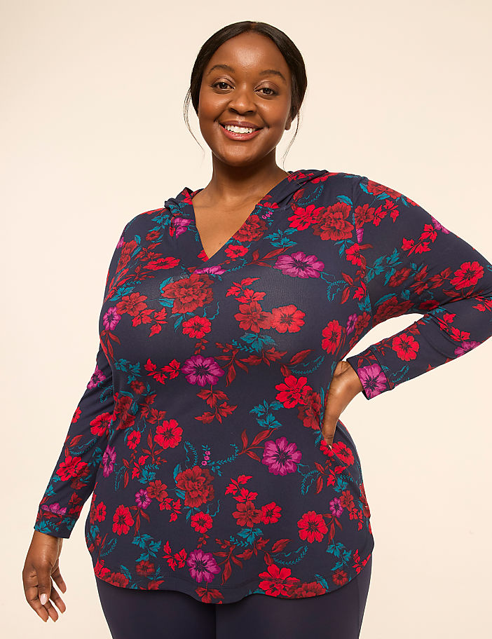 A smiling woman in a floral hoodie stands against a plain, light-colored background.