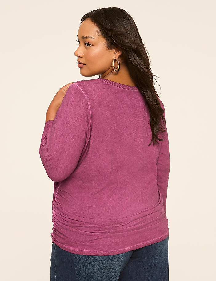 A woman in a purple top and jeans stands against a plain, light-colored background.