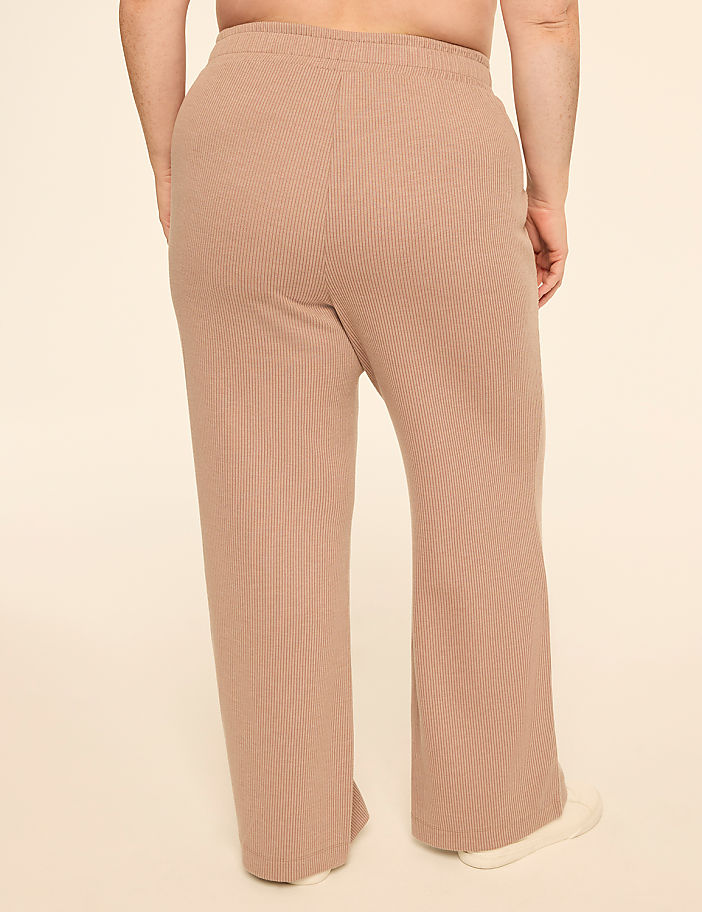 A person wearing tan ribbed lounge pants stands against a plain cream background.
