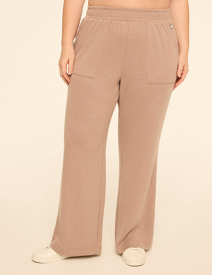 A person wearing tan, wide-leg, ribbed pants with white sneakers stands against a plain, light-colored background.