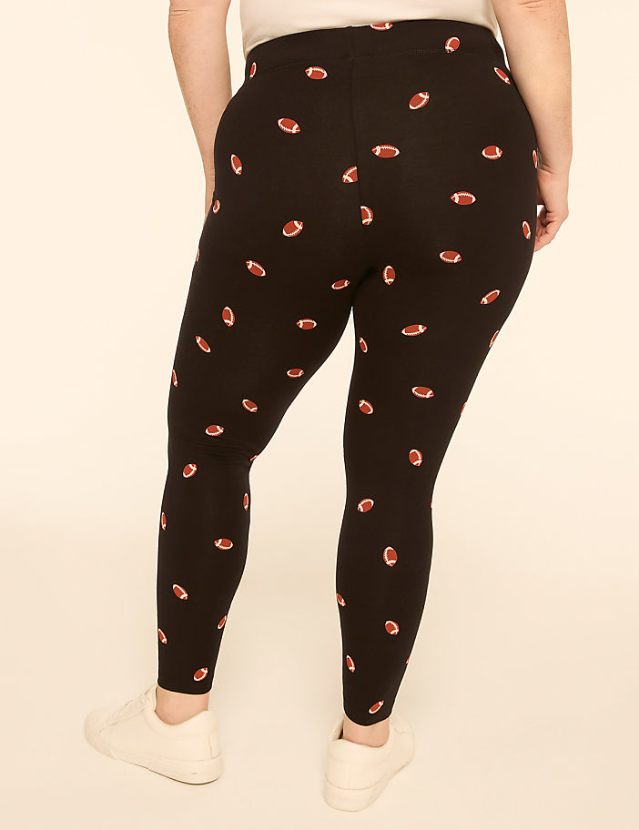 A person wearing black leggings with a football pattern stands against a plain, light-colored background.