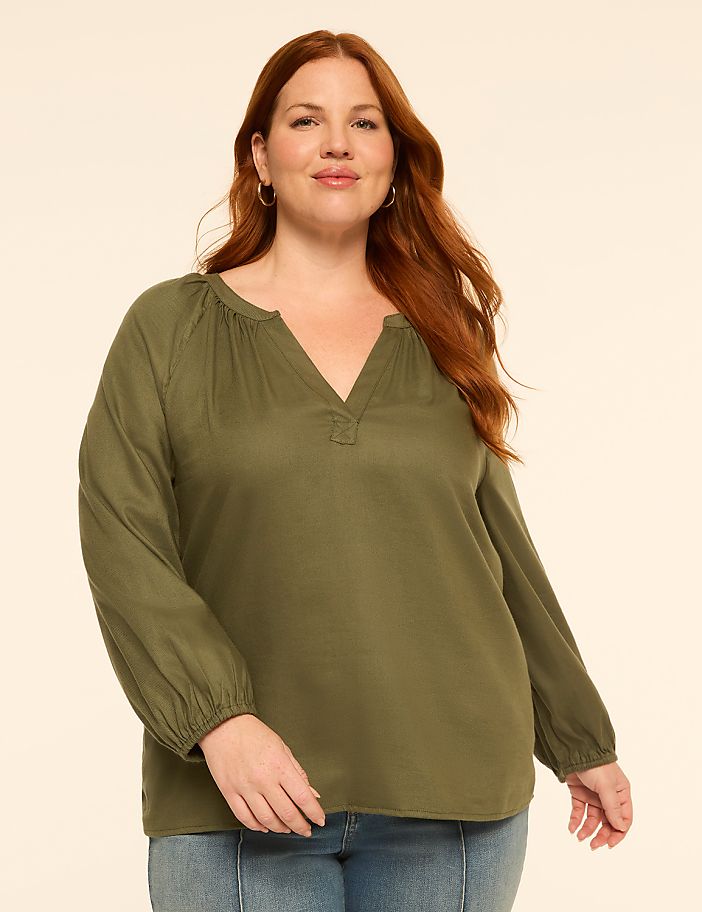A woman with red hair and a green blouse stands against a plain, light-colored background.
