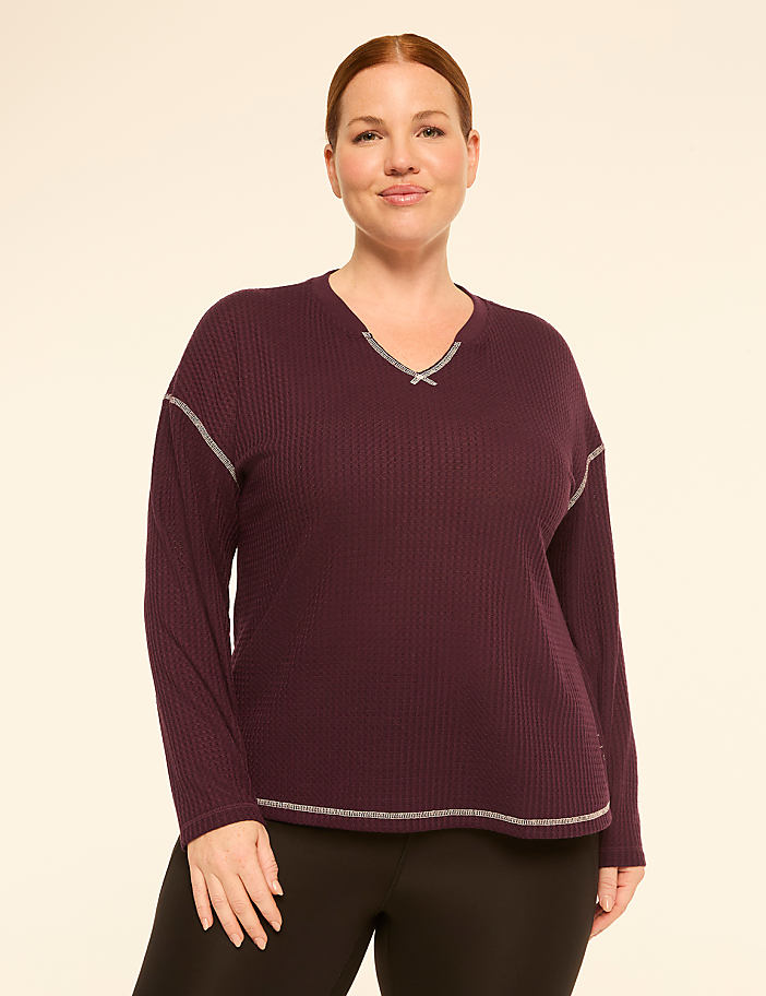 A woman in a plum waffle-knit top and black leggings stands against a plain, light beige background.