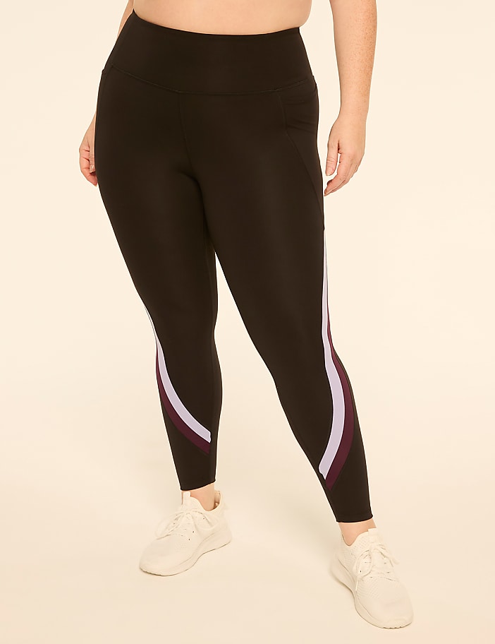 A person wearing black leggings with colored stripes on the legs stands against a plain, light-colored background.