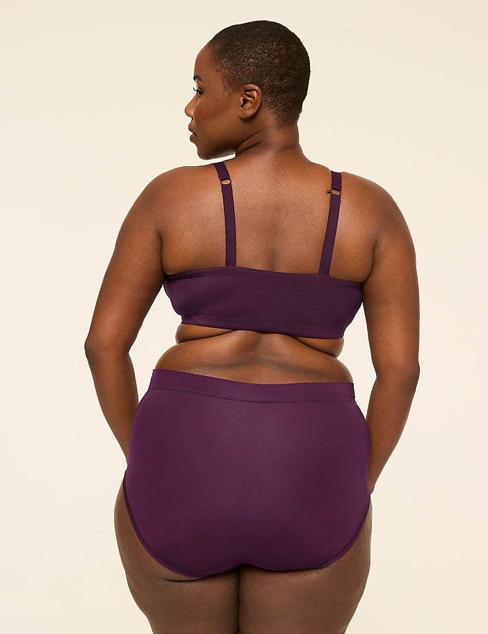 A woman in purple undergarments stands with her back to the viewer against a plain, light-colored background.