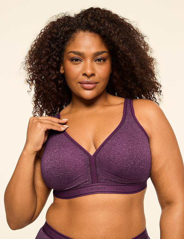 A woman with curly dark hair and a purple bra is posed against a plain, light-colored background.