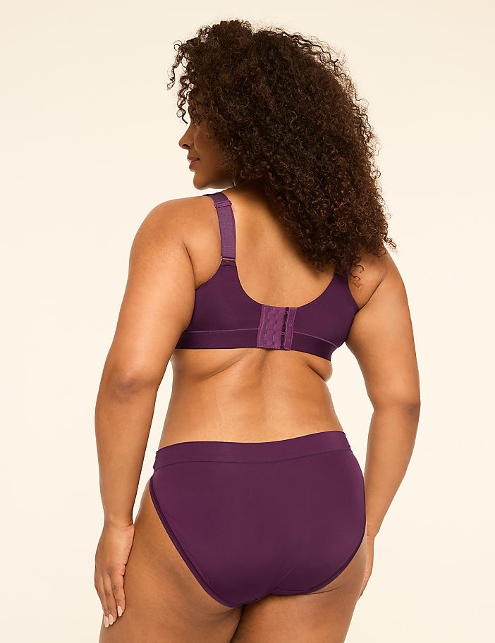 A woman in a purple bra and underwear stands against a plain, light-colored background.