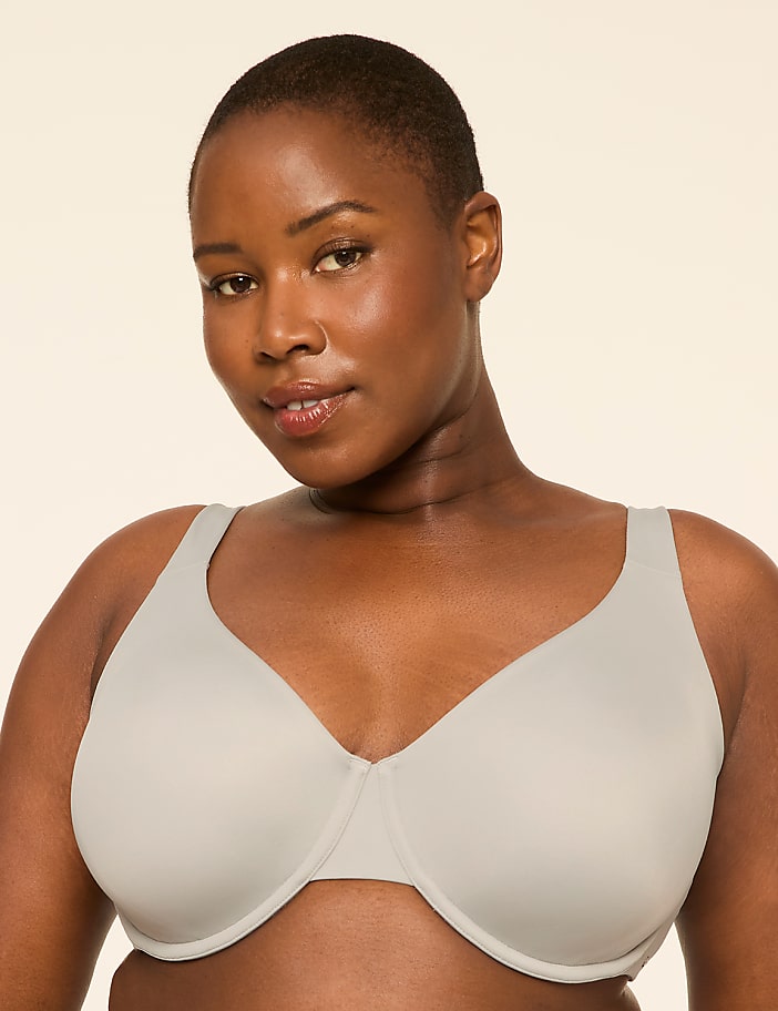 A woman with short hair and a light gray bra is centered against a plain, light-colored background.