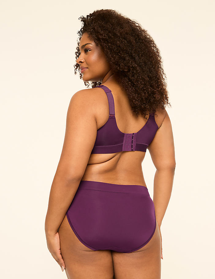 A woman in a purple bra and underwear stands against a plain, light-colored background.