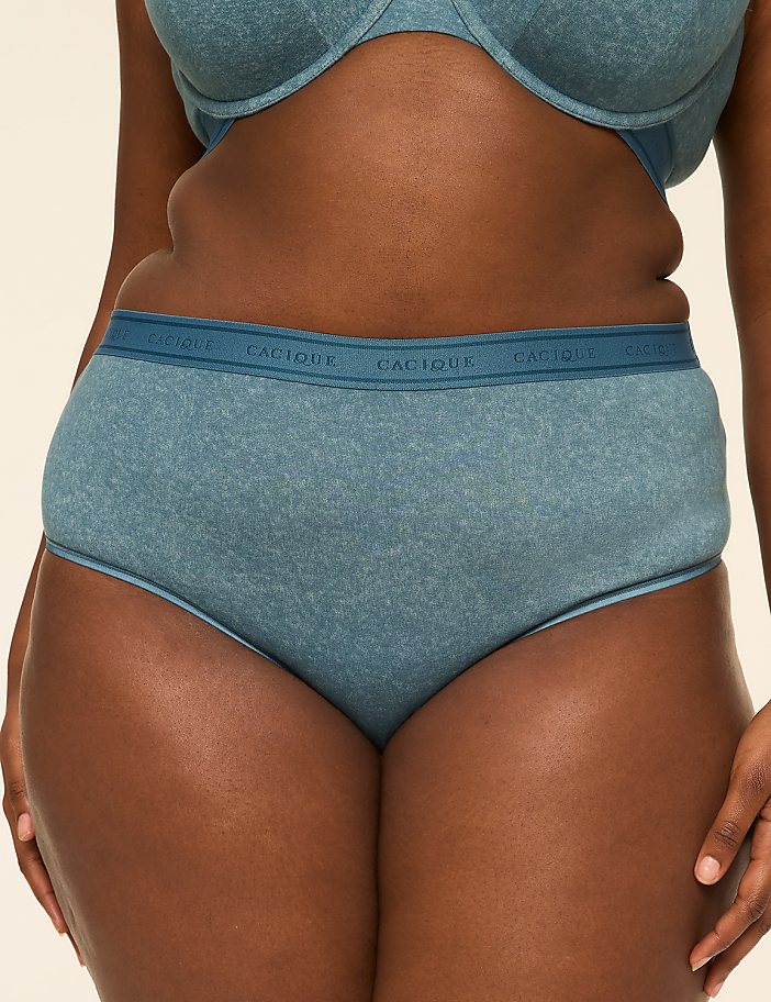 A person wears blue cotton underwear and a matching bra against a plain, light-colored background.