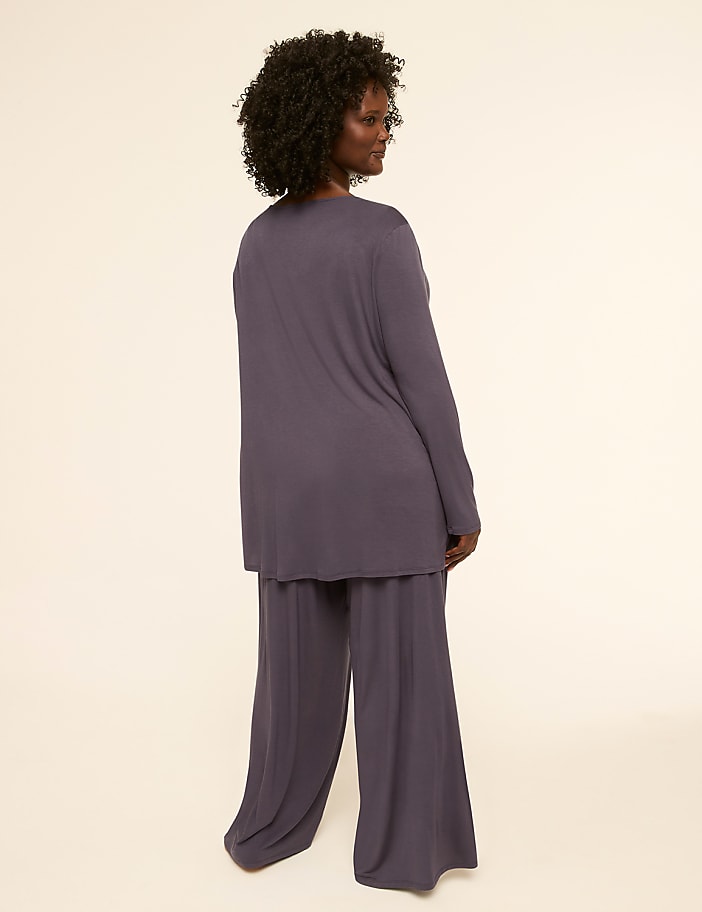 A woman in a purple loungewear set stands against a plain, light-colored background.