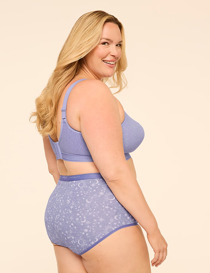 A smiling woman in a purple bra and patterned underwear is shown against a plain, light background.