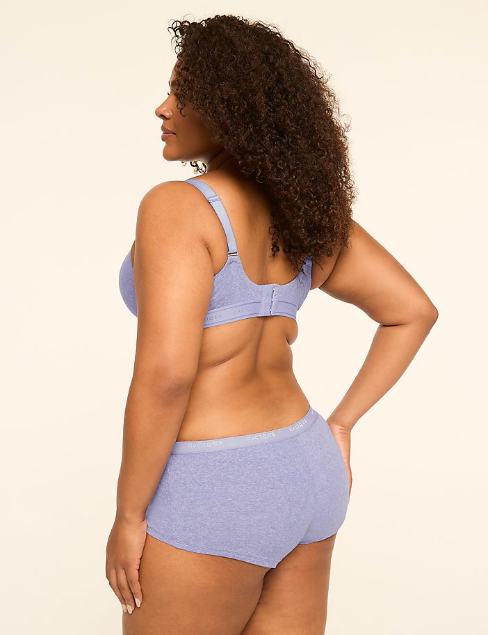 A woman in a light purple bra and matching underwear stands with her back to the viewer against a plain, light-colored background.