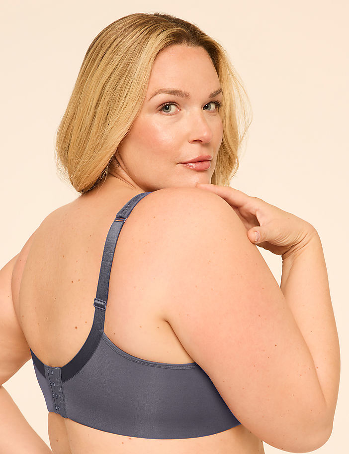 A woman in a gray bra turns her head to look over her shoulder against a plain, light-colored background.