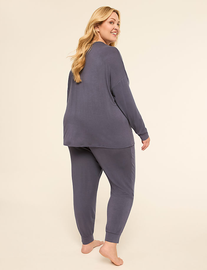 A woman in a blue loungewear set stands barefoot against a plain, light-colored background.