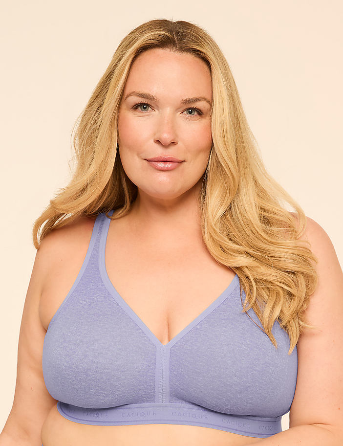 A woman with blonde hair smiles gently in a light purple bra against a plain, light background.