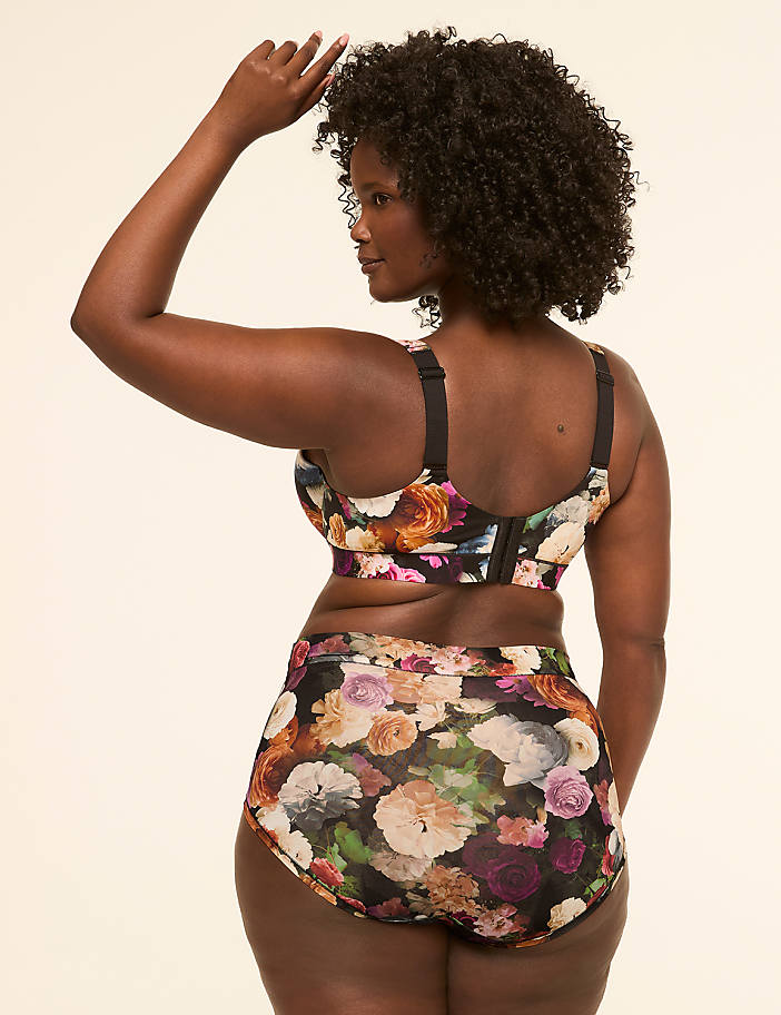 A woman in a floral bra and high-waisted underwear stands against a plain, light-colored background.