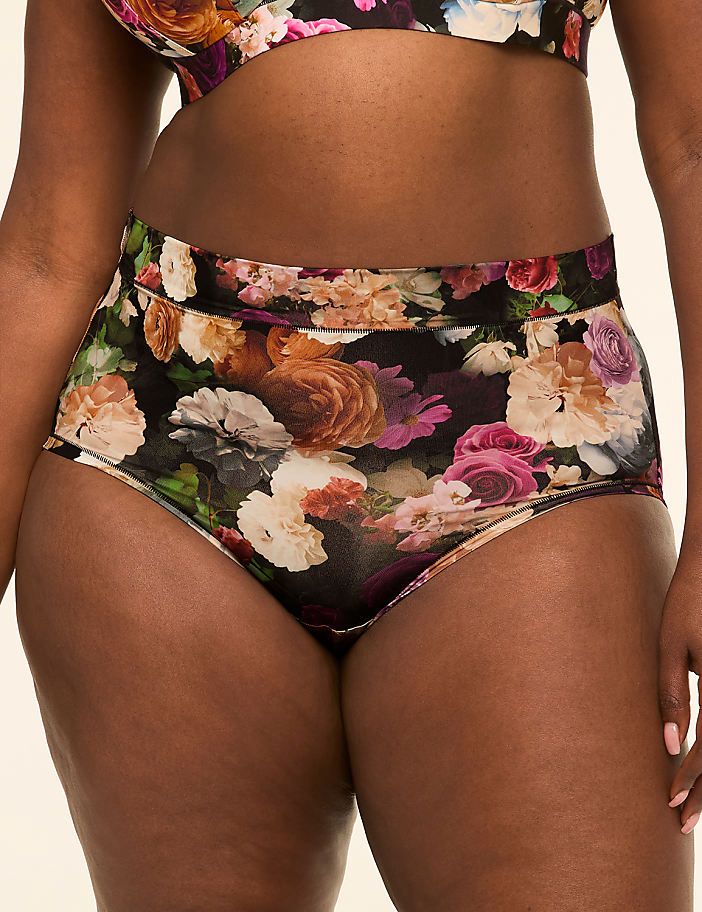 A person wears high-waisted underwear with a vibrant floral pattern against a plain background.