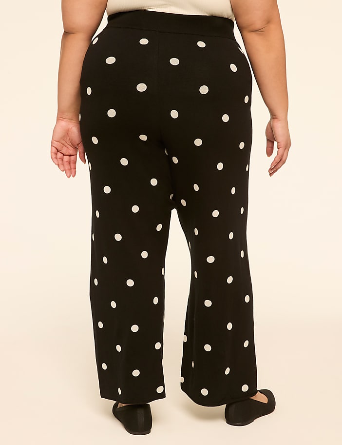 A person wearing black polka dot pants stands against a plain, light-colored background.