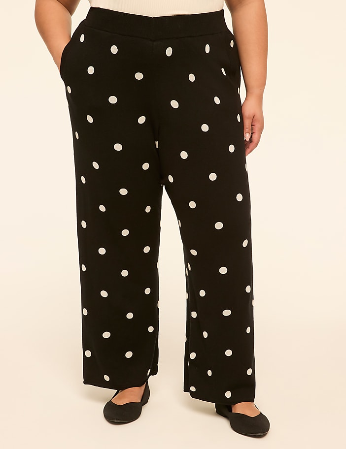A person stands in black polka dot pants and black flats against a plain, light-colored background.