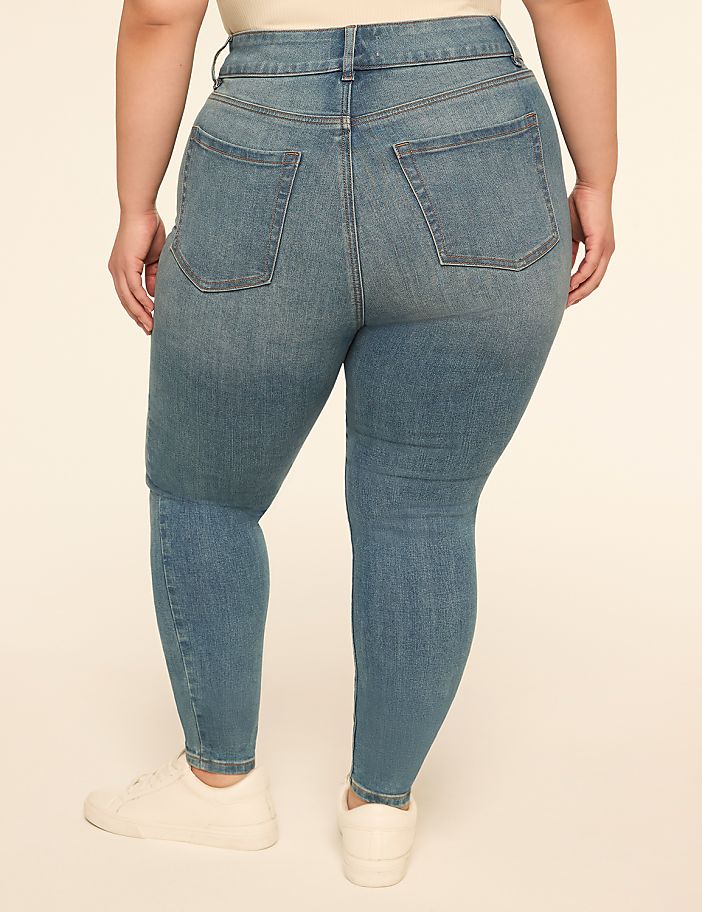 A person wearing blue denim jeans and white sneakers stands against a plain, light-colored background.
