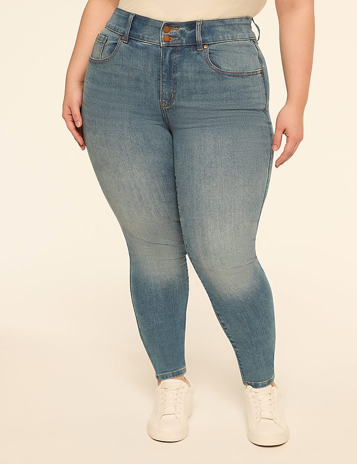 A person wearing light blue denim jeans and white sneakers stands against a plain, light-colored background.