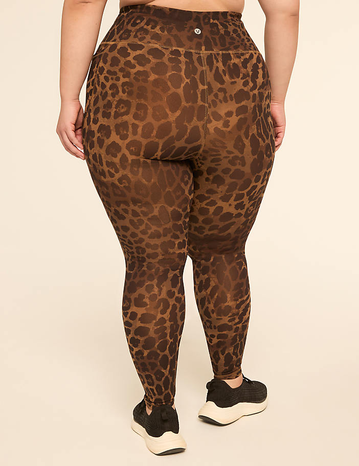 A person wearing leopard print leggings and black sneakers stands against a plain, light-colored background.