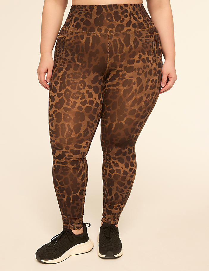 A person wearing leopard-print leggings and black sneakers stands against a plain, light-colored background.