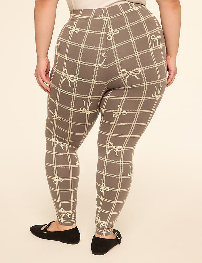 A person wearing plaid leggings with a bow pattern stands on a plain cream-colored background.