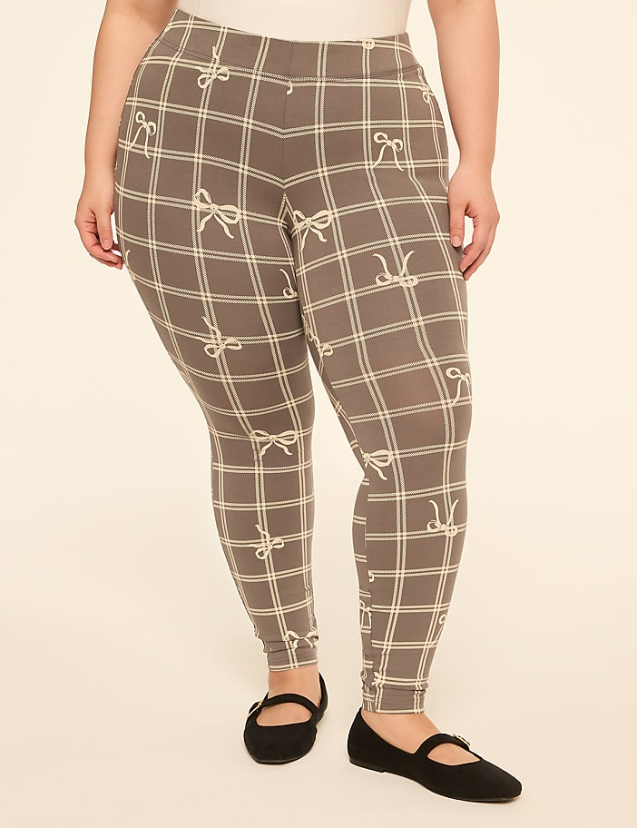 A person wearing grey plaid leggings with a bow pattern stands against a plain, light-colored background.