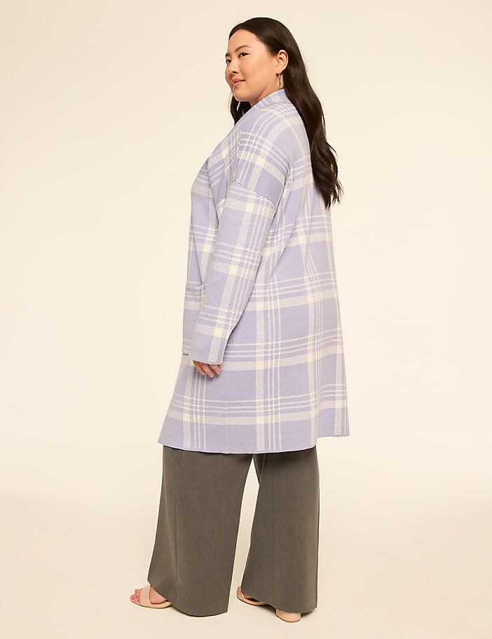 A woman in a plaid coat and wide-leg pants stands against a plain, light-colored background.