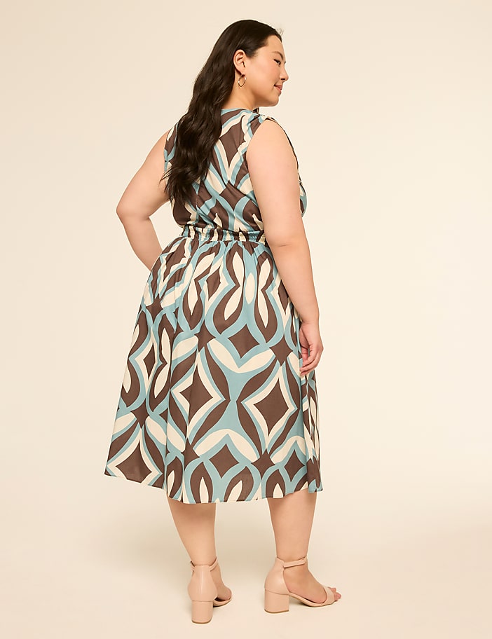 A woman in a patterned dress stands against a plain, light-colored background.