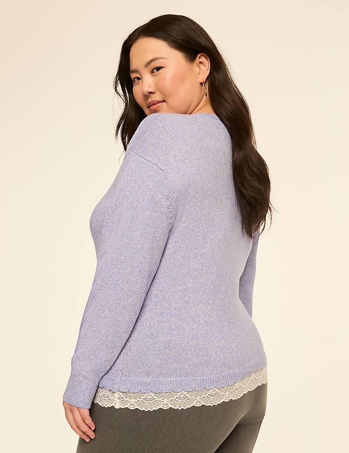 A woman in a light purple sweater with lace trim stands against a plain, light-colored background.