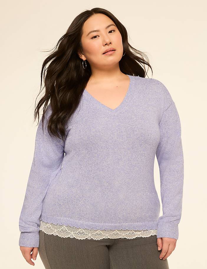 A woman in a light purple v-neck sweater layered over a white lace-trimmed camisole stands against a plain beige background.